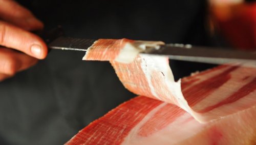 Uomo taglia una fetta di prosciutto crudo.