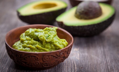 Una ciotola di aguacate e un avocado tagliato dietro