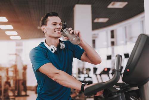 Benefici dell'acqua alcalina. Ragazzo beve in palestra