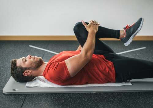 Uomo che fa stretching per allungare il gluteo portando il ginocchio al petto.